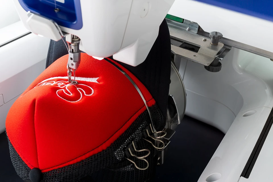 Atelier de broderie industrielle avec machine à broder automatisée travaillant sur une casquette rouge et noire